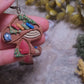 video close up of Mushroom Shelf Earring on a stone background surrounded by foliage. 