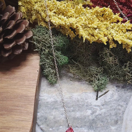 video of Necklace with colorful triangle pendants on a stone surface with plants in the background