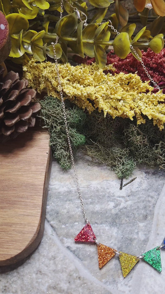 video of Necklace with colorful triangle pendants on a stone surface with plants in the background
