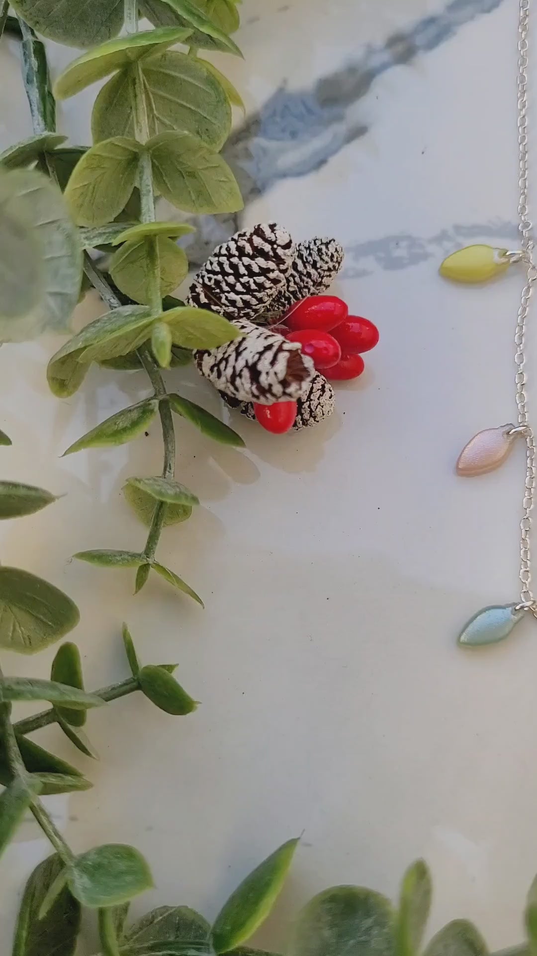 video close up of Christmas lights necklace on a marble background surrounded by foliage.