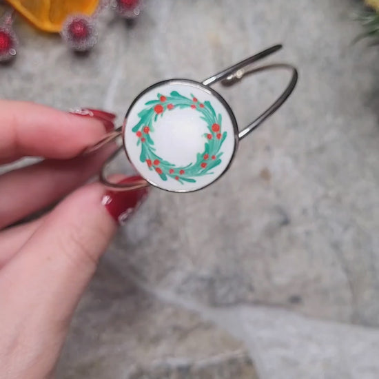 Video close up of silver holly bracelet on a wood and stone background surrounded by foliage. 