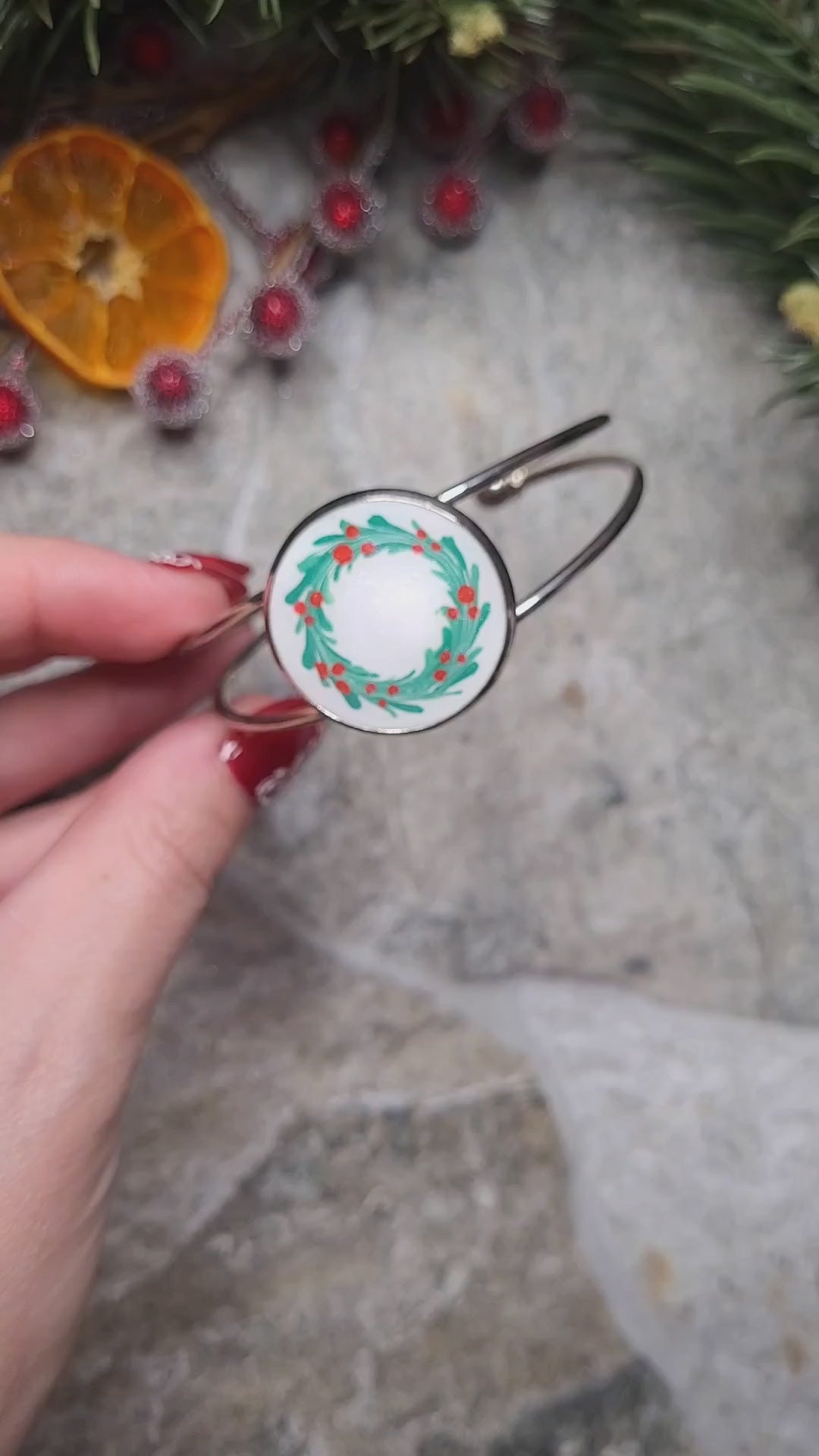 Video close up of silver holly bracelet on a wood and stone background surrounded by foliage. 