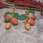 video close up of 3d acorn shaped earrings with  oak leaves. Sitting on a stone background surrounded by foliage. 