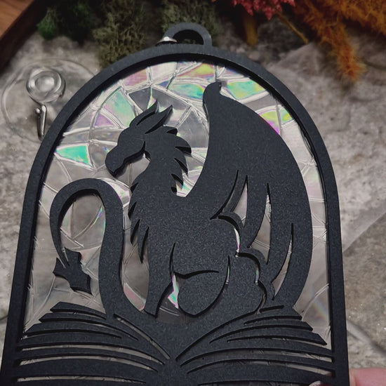 video of Book Dragon suncatcher on a stone background surrounded by foliage

