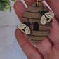 video close up of wooden beehive shaped earrings with bee charms on a marble background surrounded by foliage.