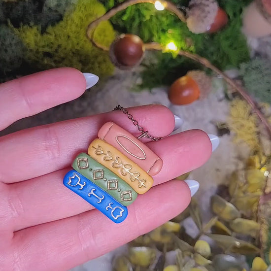 video close up of Gilded bookstack necklace on stone background surrounded by moss and foliage