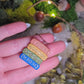 video close up of Gilded bookstack necklace on stone background surrounded by moss and foliage