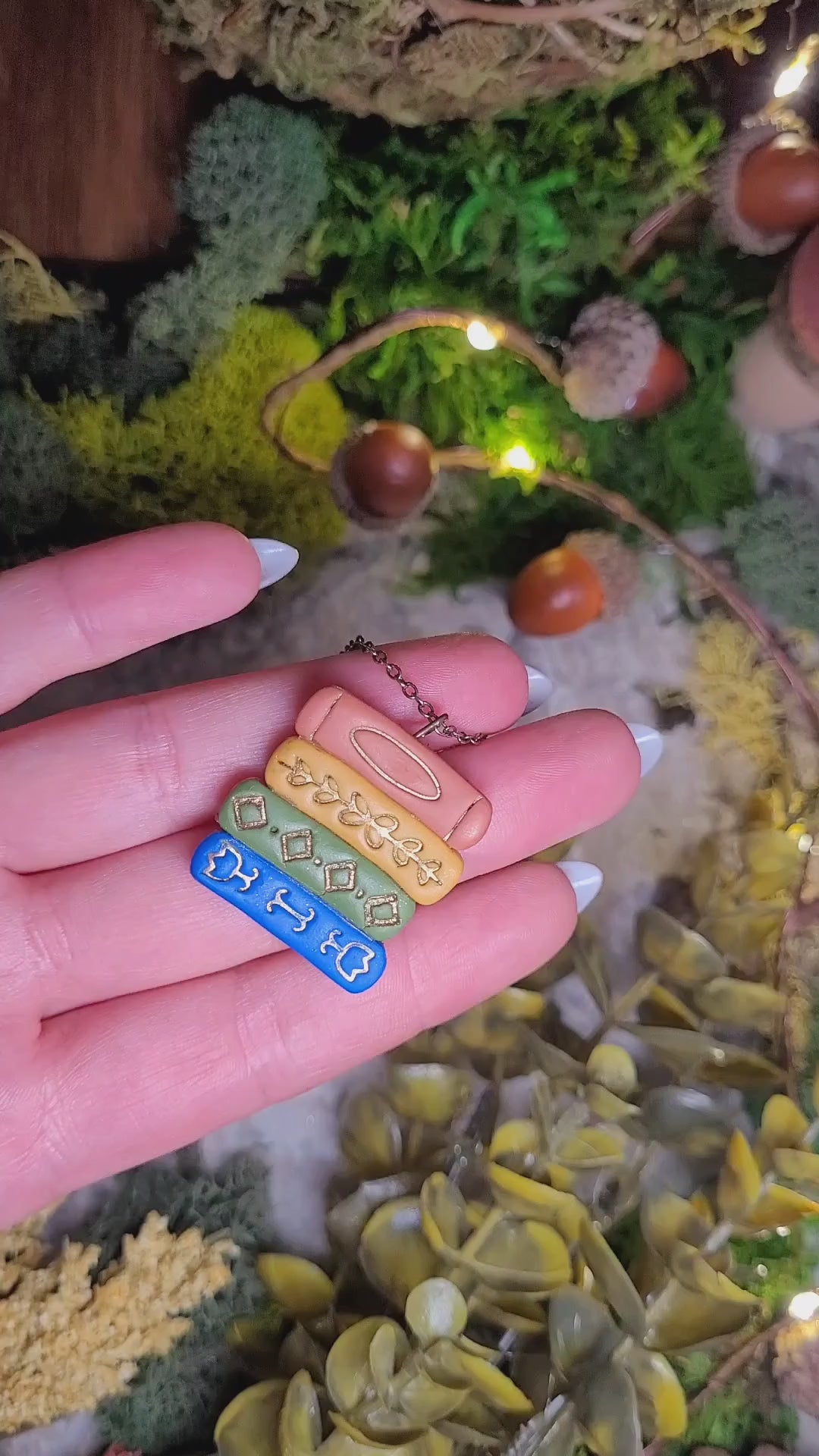 video close up of Gilded bookstack necklace on stone background surrounded by moss and foliage