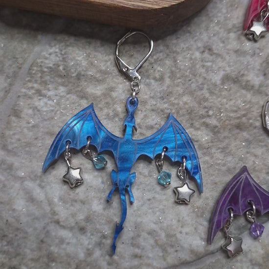 video of 10 colors of dragon dangles on a stone background surrounded by foliage. 