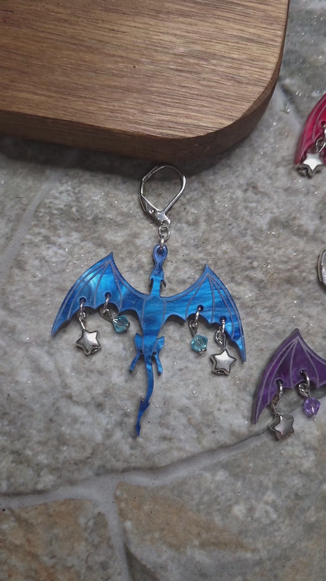 video of 10 colors of dragon dangles on a stone background surrounded by foliage. 