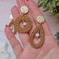 video close up of tear drop and round rattan earrings on a marble background with foliage.