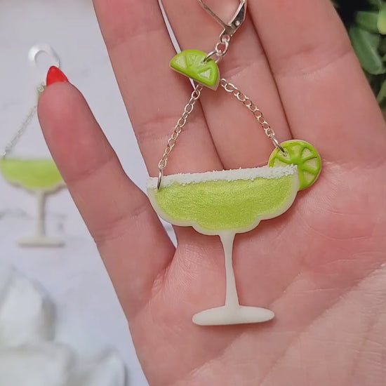 video close up of Lime margarita glass earrings on a marble background with foliage. 