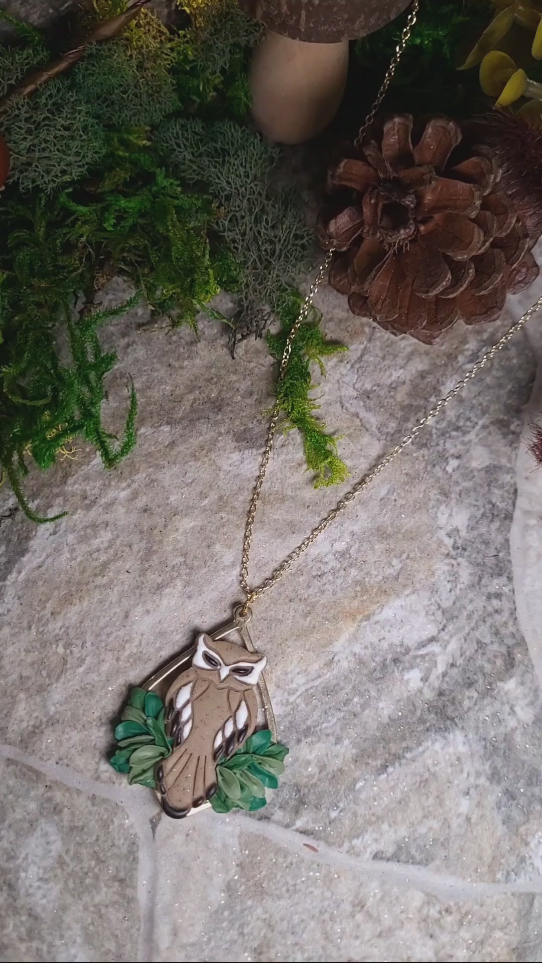 video close up of Owl necklace sitting on a stone background surrounded by foliage. 