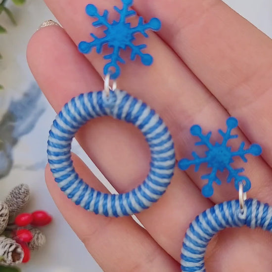 video close up of snowflake striped hoop earrings on a white marble background surrounded by foliage.