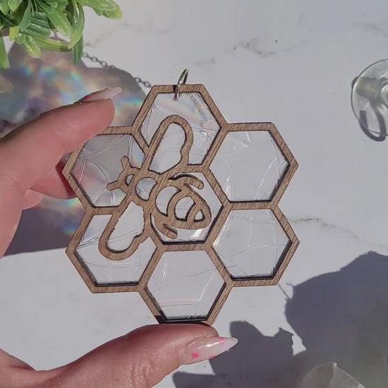 video or Bee suncatcher on marble background surrounded by foliage.