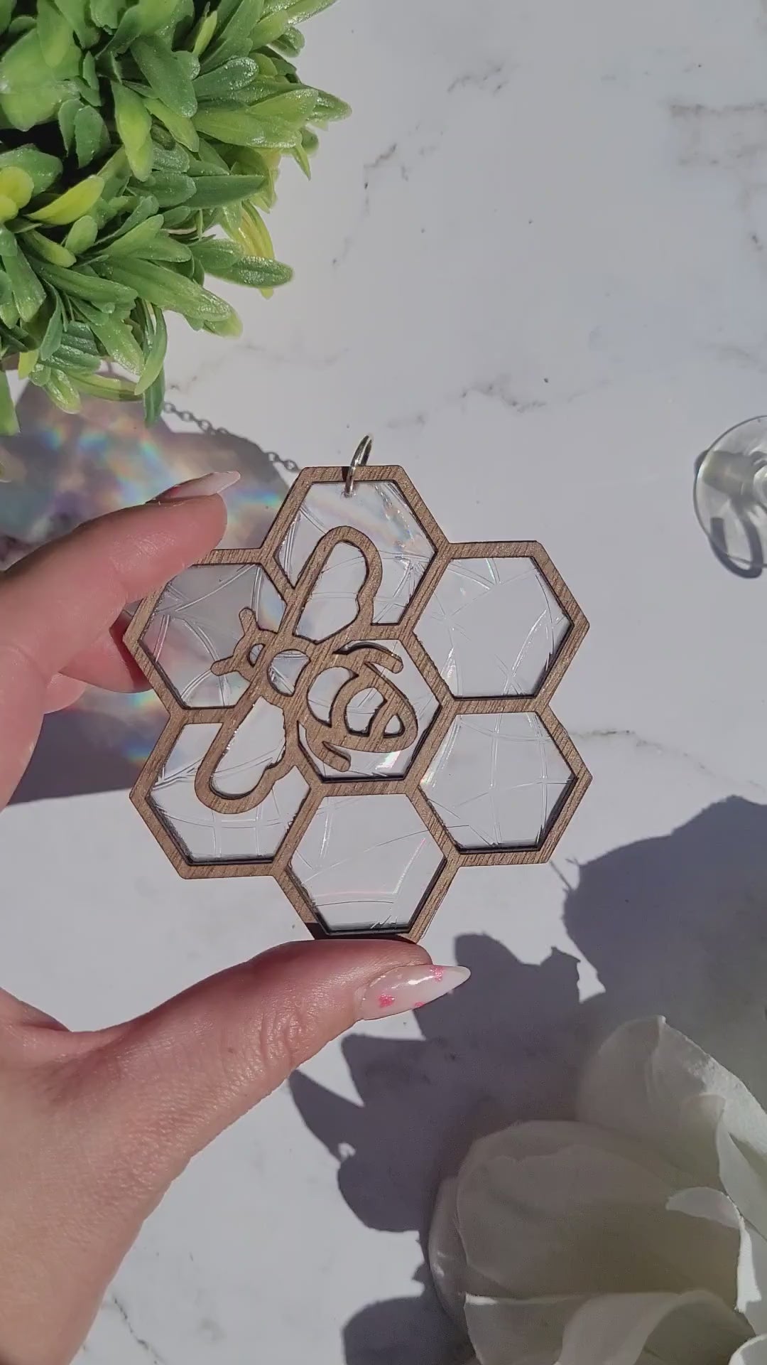 video or Bee suncatcher on marble background surrounded by foliage.