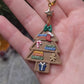 video close up of Christmas Tree Shelf Earring on a stone background surrounded by foliage. 