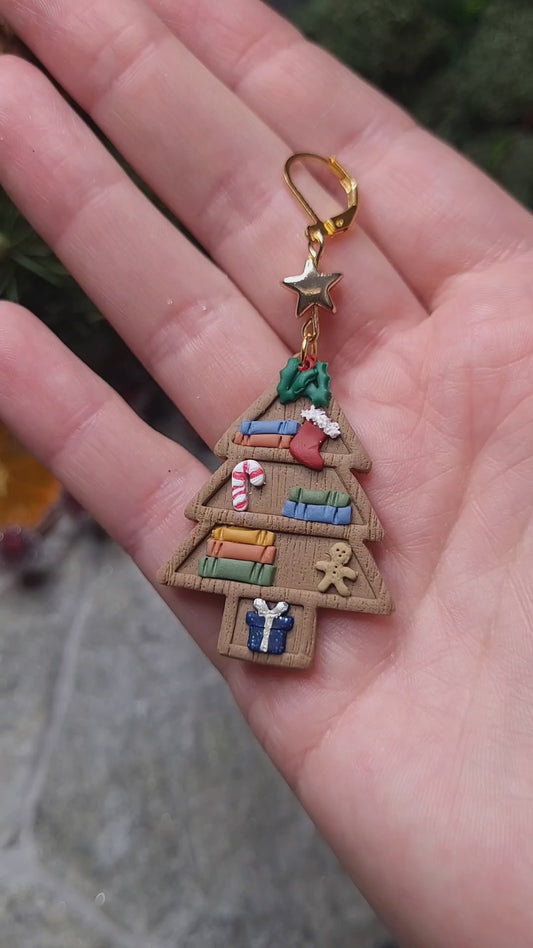 video close up of Christmas Tree Shelf Earring on a stone background surrounded by foliage. 