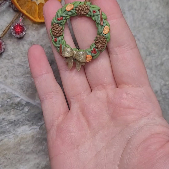 video close up of Holiday Wreath Necklace on a stone background surrounded by foliage. 