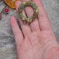 video close up of Holiday Wreath Necklace on a stone background surrounded by foliage. 