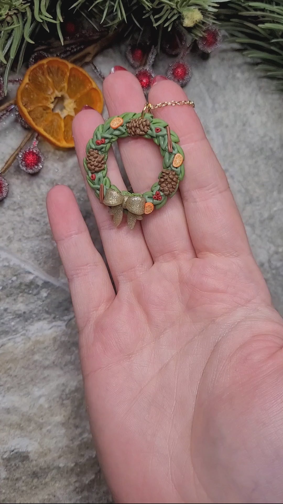 video close up of Holiday Wreath Necklace on a stone background surrounded by foliage. 