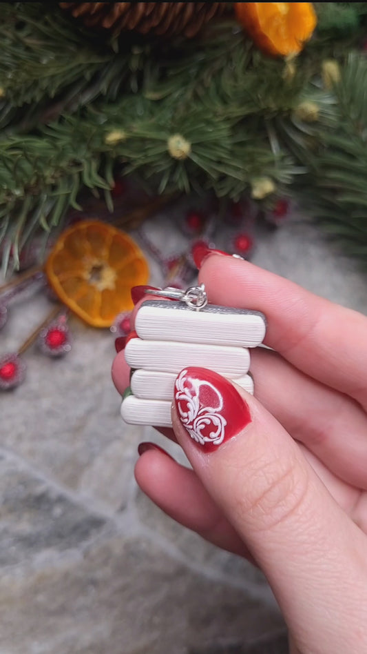 video close up of Retro Christmas Bookstack Earring on a stone background surrounded by foliage. 