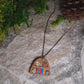 video close up of Bookshelf pendant made of polymer clay sits on a stone background surrounded by foliage. 