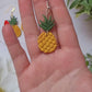 video close up of pineapple earrings on a marble background with foliage.