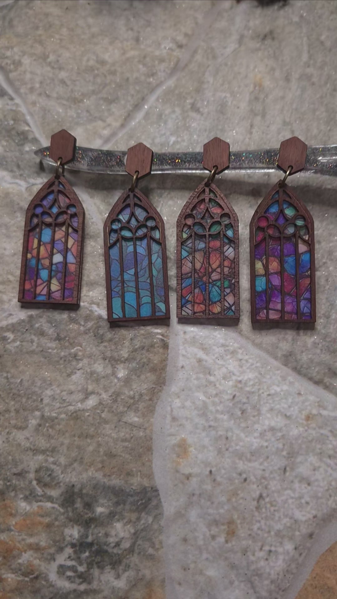 Video of 4 colors of Cathedral window earrings on a stone background surrounded by foliage.