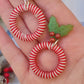 video close up of mistletoe and candy cane striped hoop earrings on a white marble background surrounded by foliage.