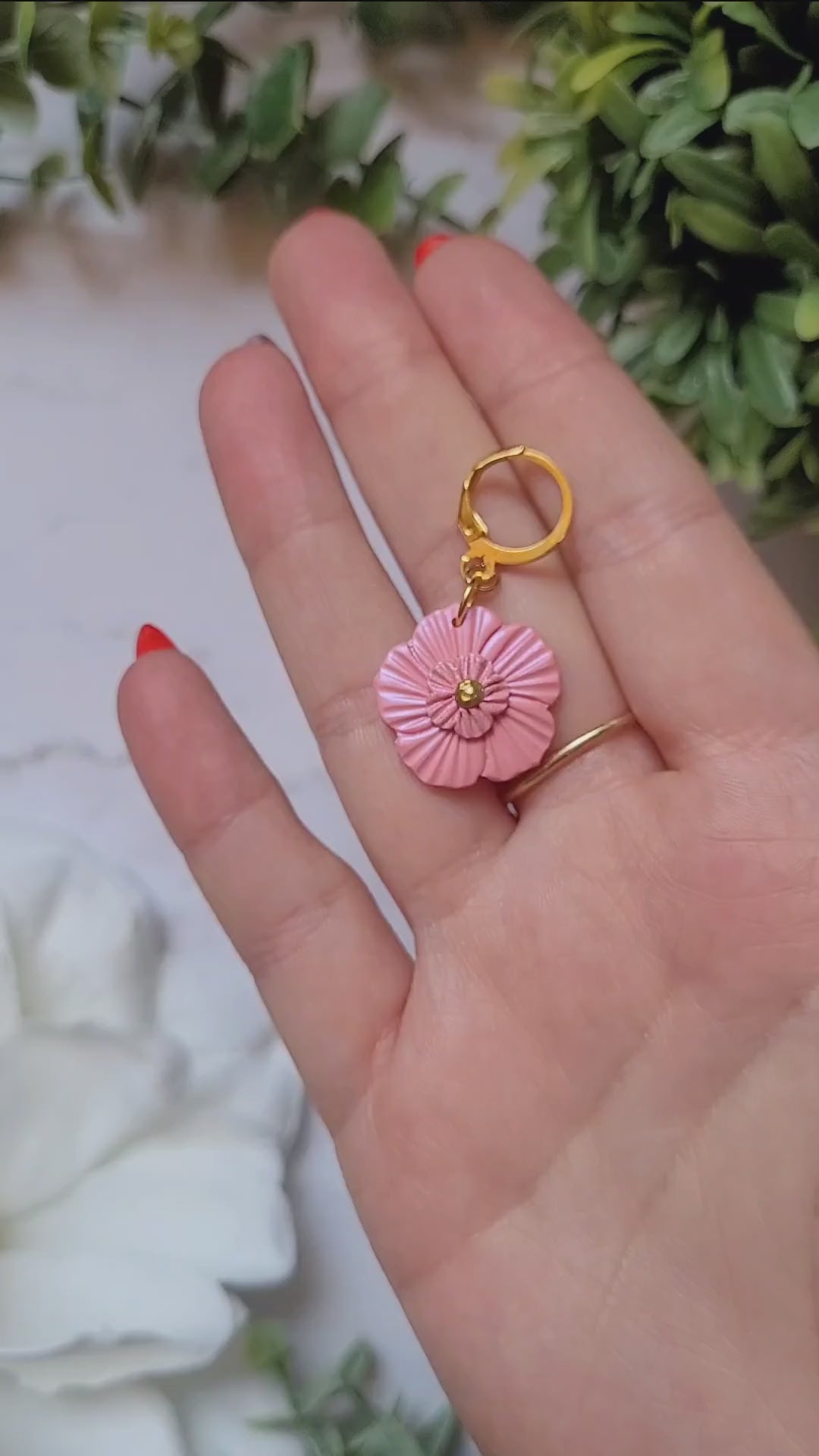 video close up of Baby pink flower earrings on white background with foliage. 