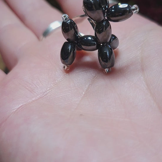 video of balloon dog earrings on a stone background surrounded by foliage. 