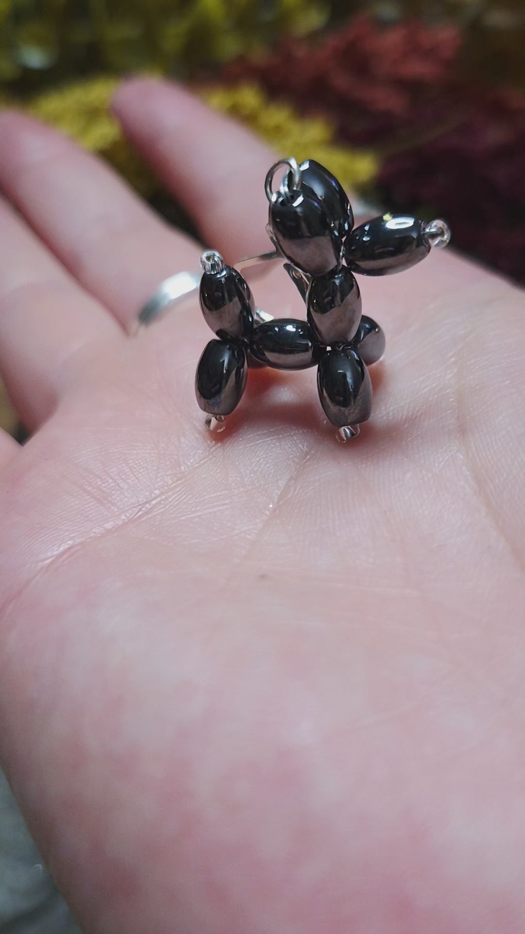 video of balloon dog earrings on a stone background surrounded by foliage. 