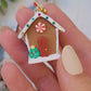 video close up of Gingerbread house earrings on a marble background surrounded by foliage.