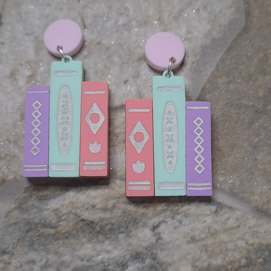 video of 2 colorways of retro book earrings on a stone background surrounded by foliage