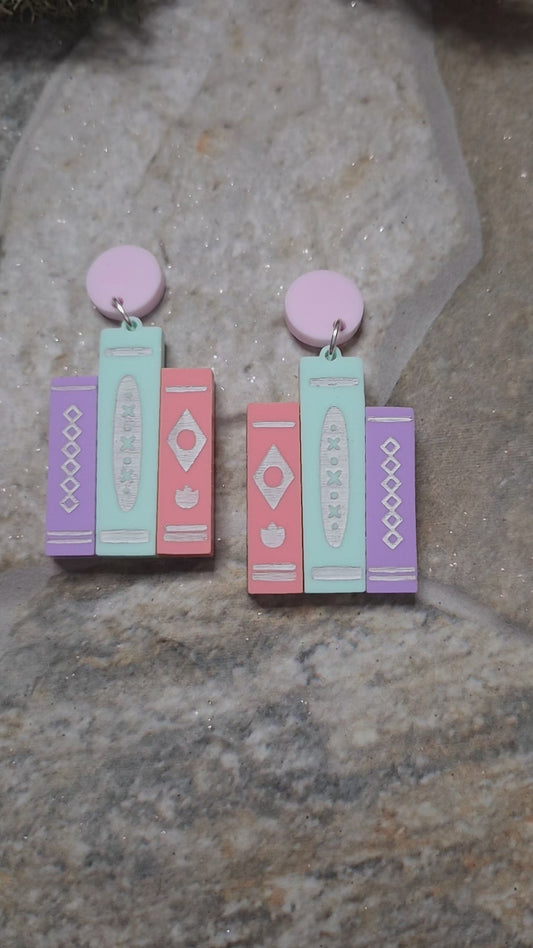 video of 2 colorways of retro book earrings on a stone background surrounded by foliage