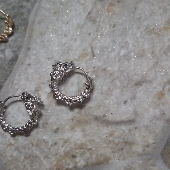 video of Gold and Silver dragon hoop earrings on a stone background surrounded by foliage