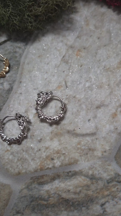 video of Gold and Silver dragon hoop earrings on a stone background surrounded by foliage