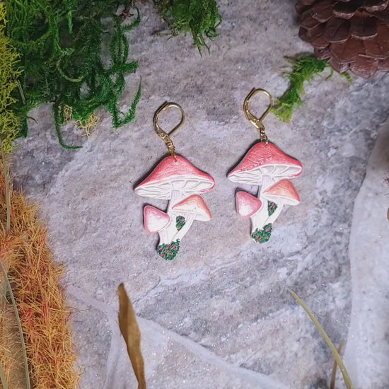 video close up of Shroom earrings on a stone background surrounded by foliage. 