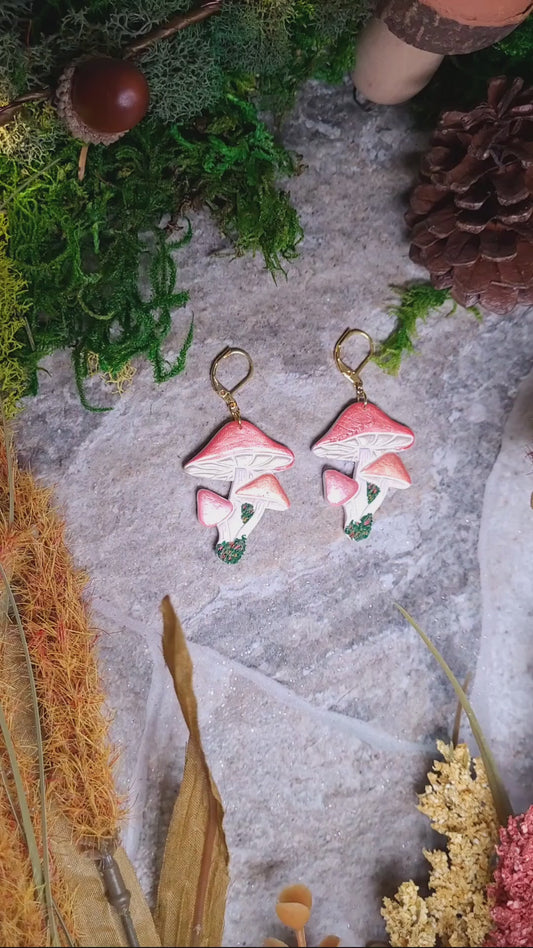 video close up of Shroom earrings on a stone background surrounded by foliage. 