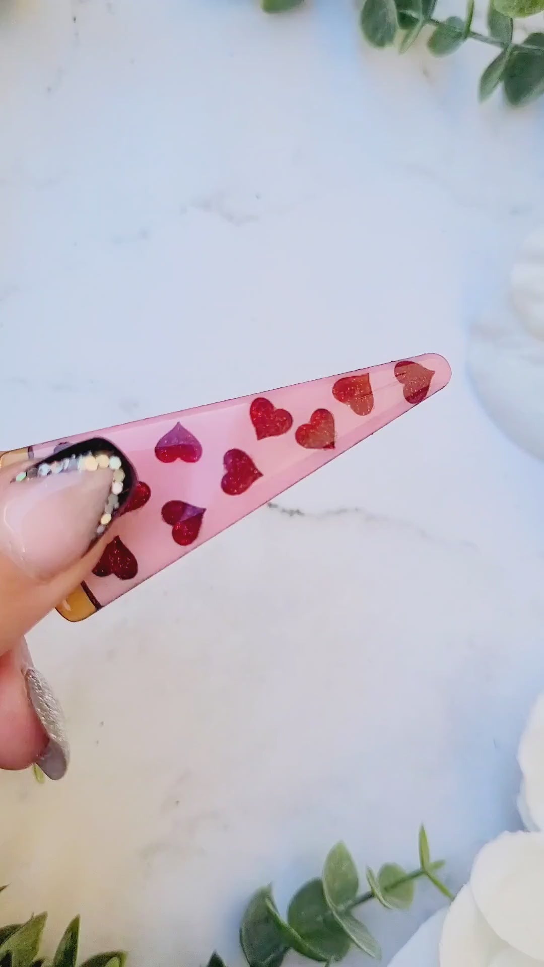 video close up of the  Slice of love pizza hair clip on a white marble background surrounded by foliage.