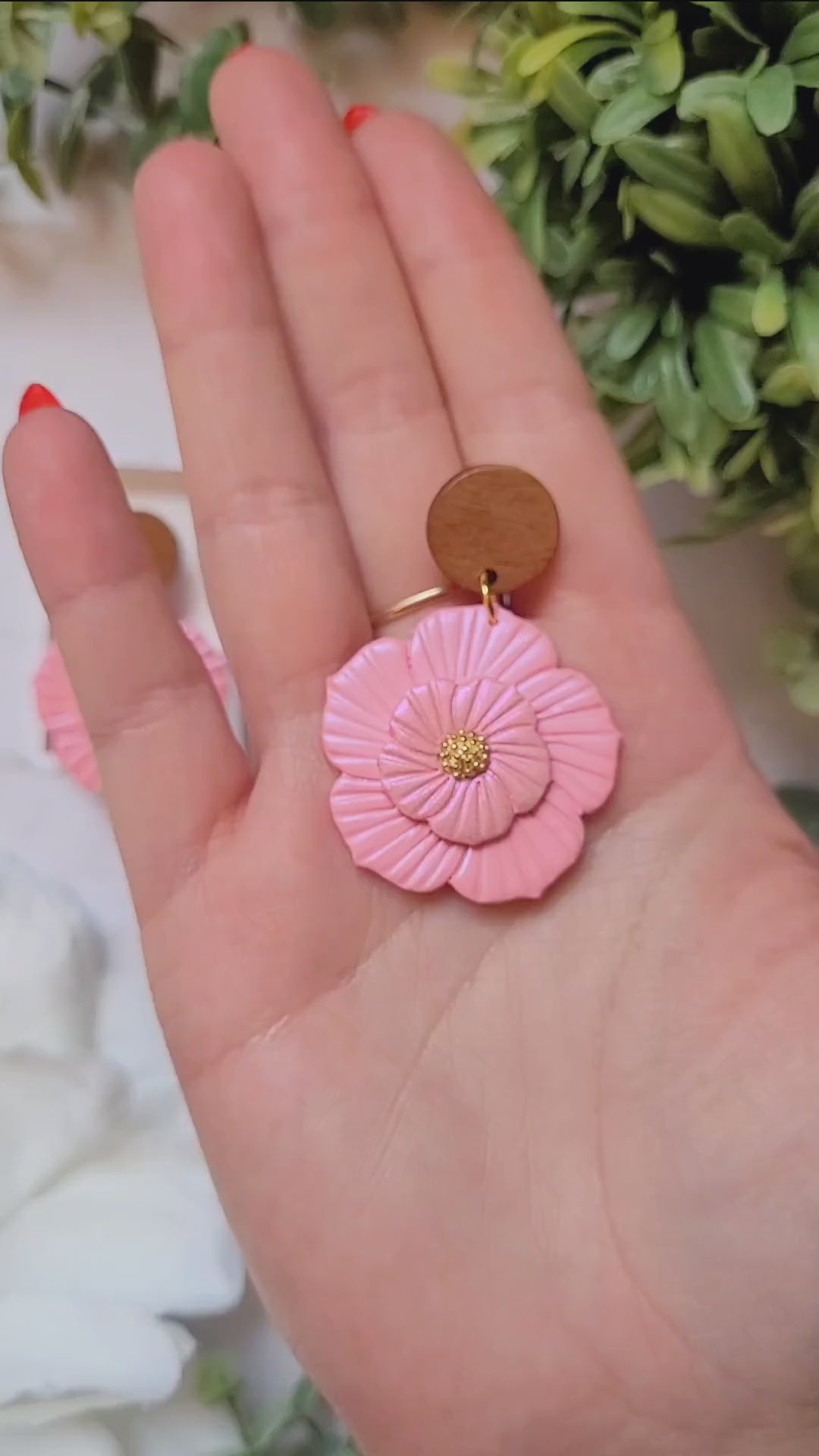 video close up of Baby pink flower earrings on white background with foliage. 