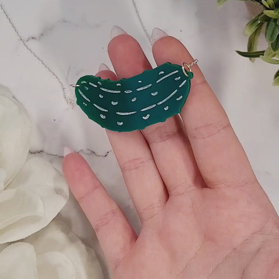 video close up of Green pickle necklace on a white marble background surrounded by foliage.