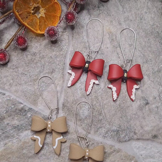 video close up of Christmas Bow earrings on a  stone background surrounded by foliage