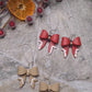 video close up of Christmas Bow earrings on a  stone background surrounded by foliage