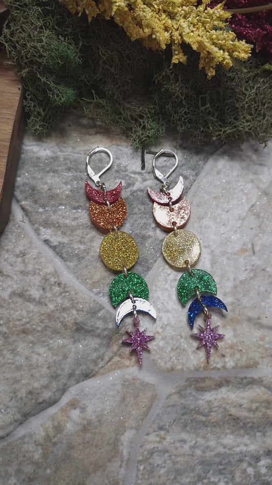 video of Rainbow moon phase earrings on a stone background surrounded by foliage 