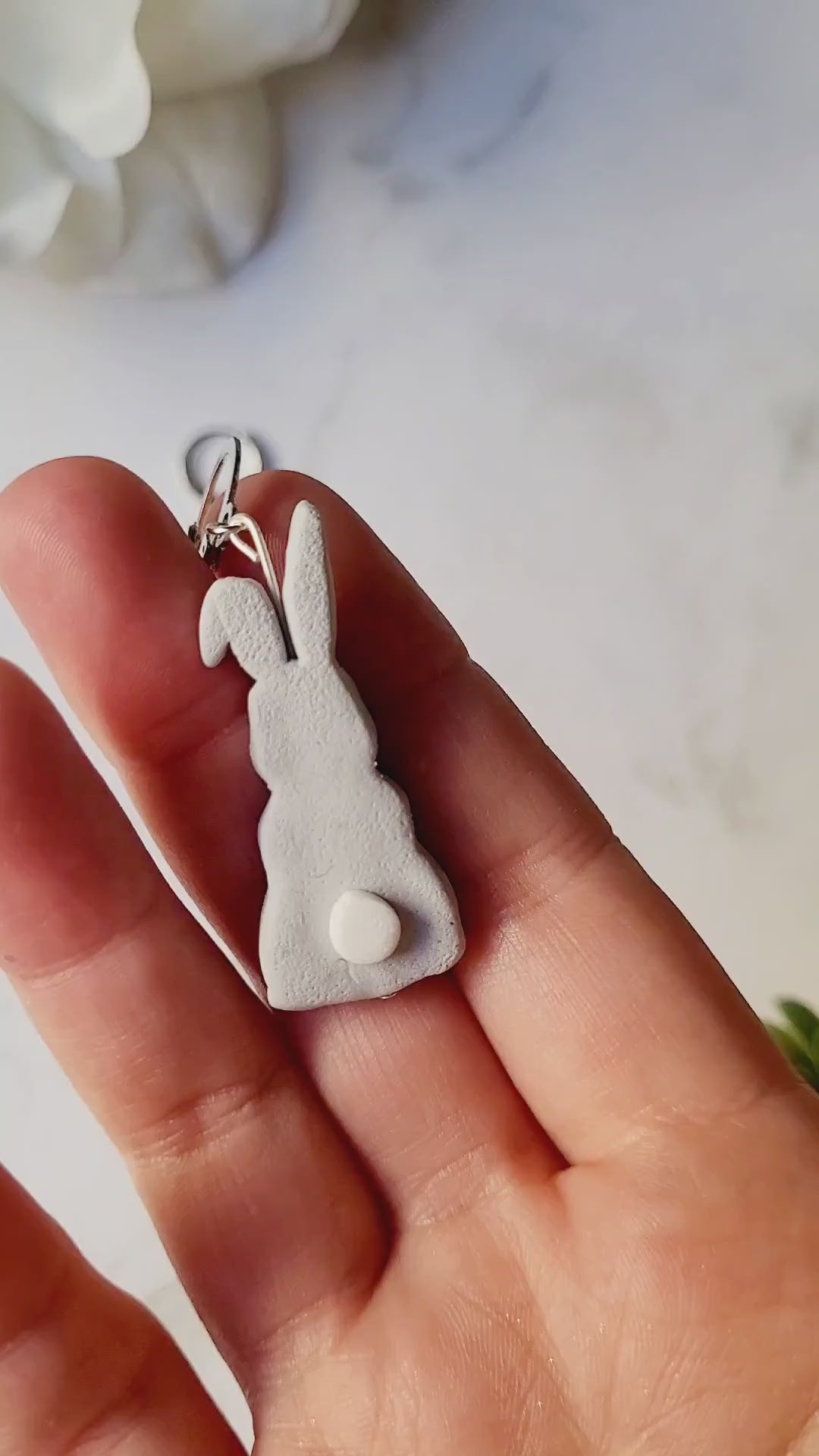 video close up of grey bunny earrings. 