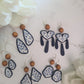5 styles of polymer clay earrings on a white background. Earrings are white and navy with a tile print and wood bead. 