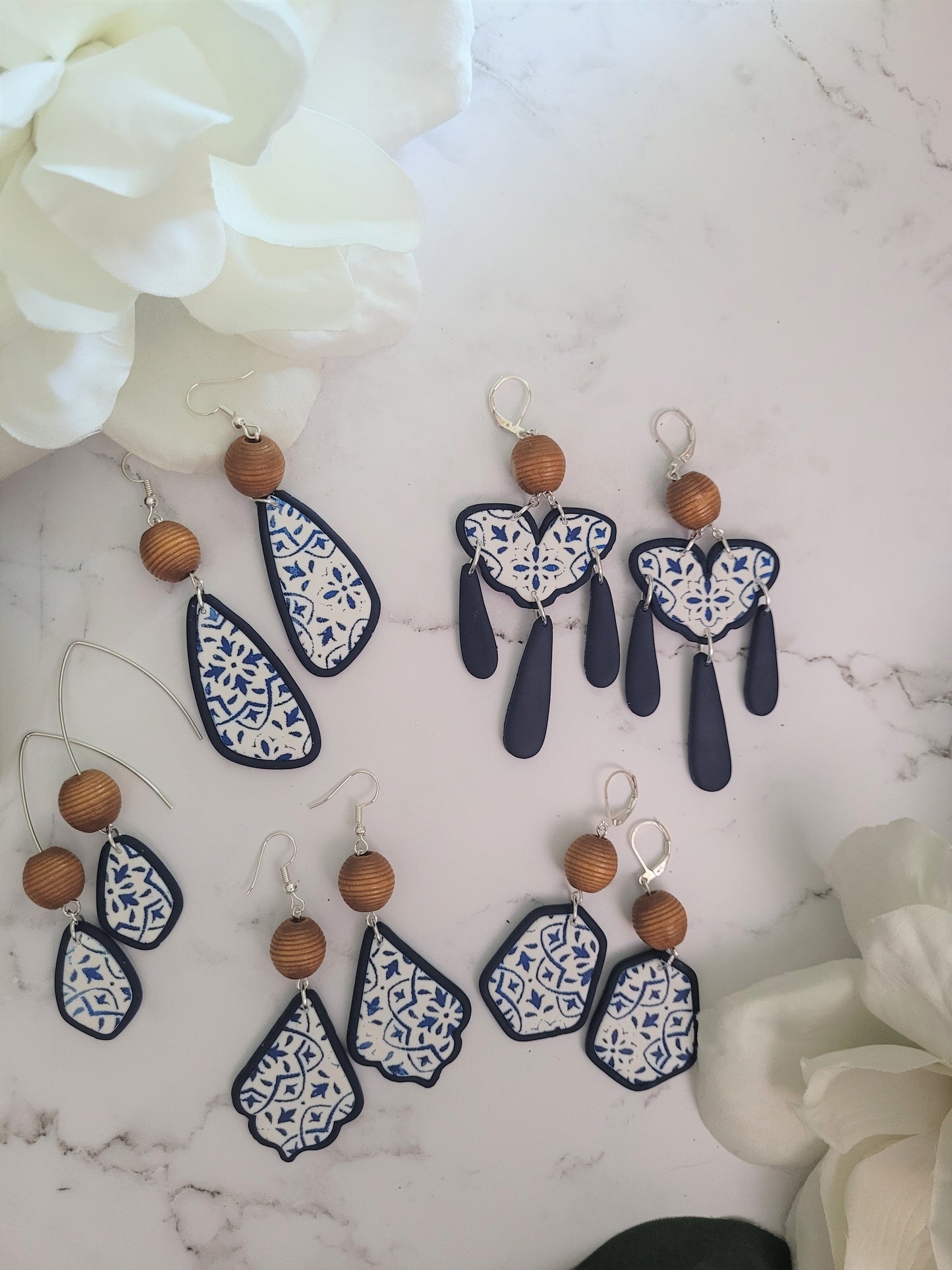5 styles of polymer clay earrings on a white background. Earrings are white and navy with a tile print and wood bead. 