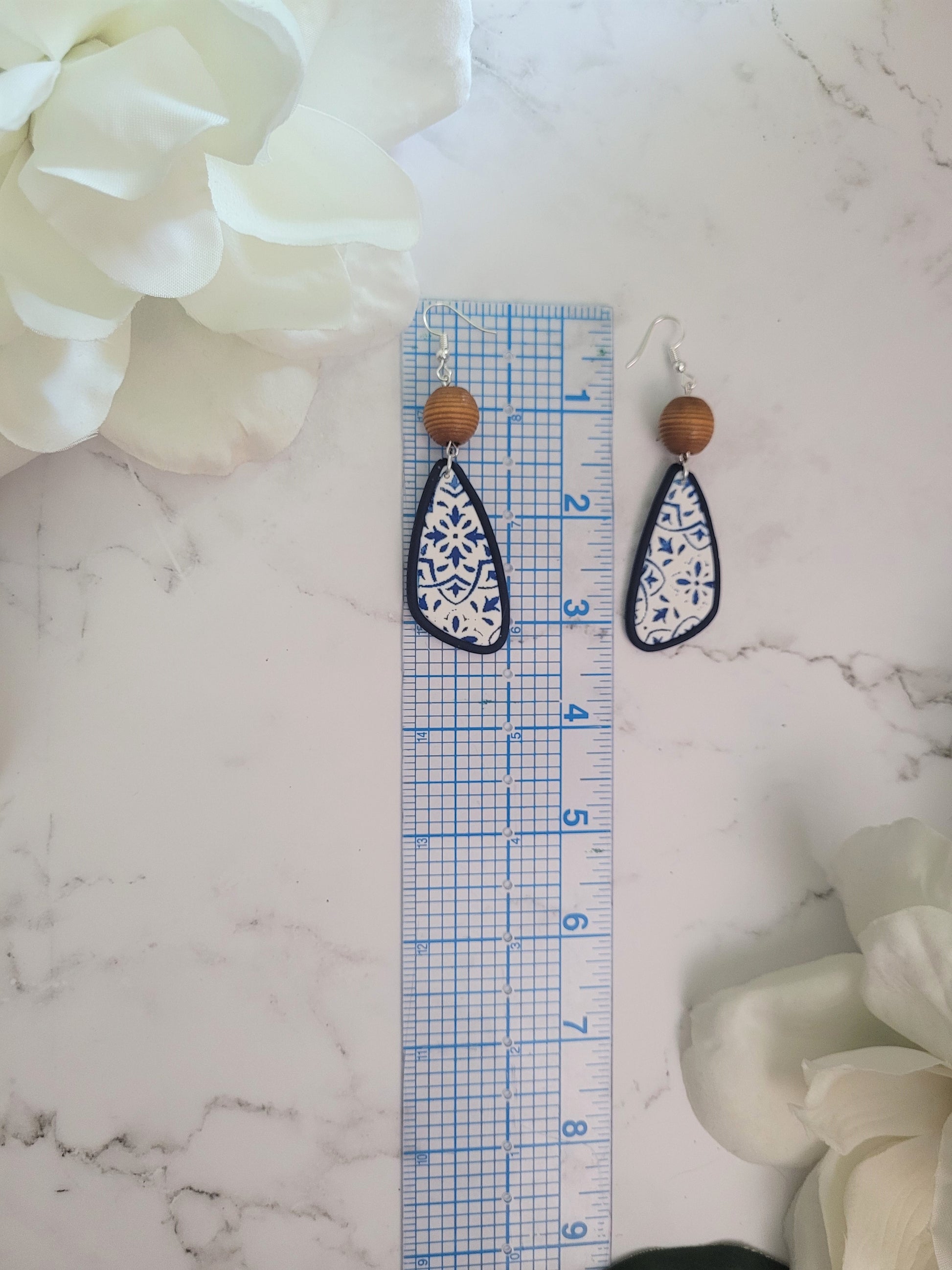 Closeup of Riley style polymer clay earrings on a white background. Earrings are white and navy with a tile print and wood bead.